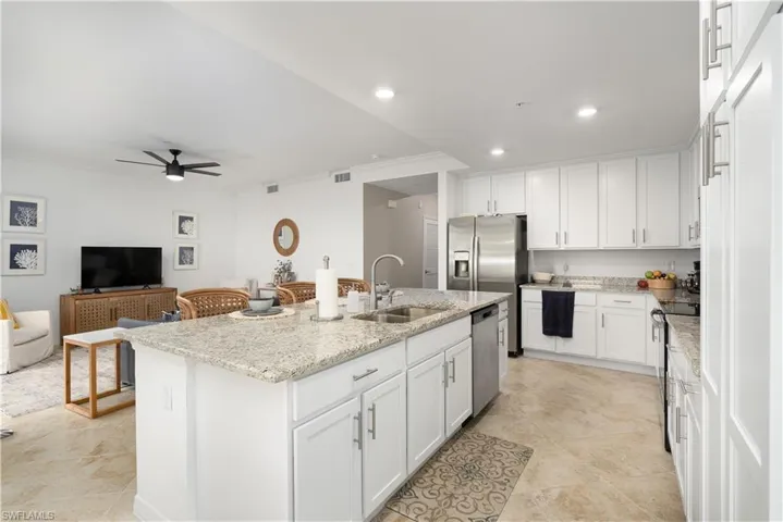Kitchen with white cabinets, stainless steel appliances, sink, a kitchen island with sink, and light stone counters