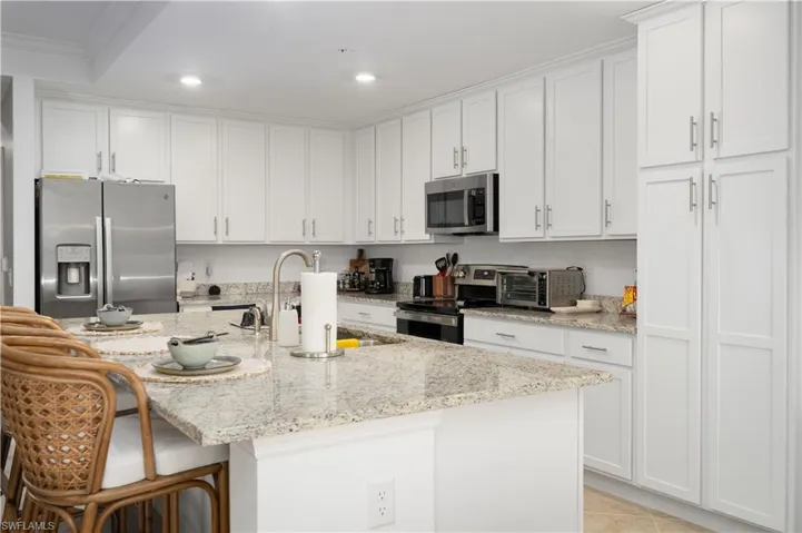 Kitchen with white cabinets, appliances with stainless steel finishes, an island with sink, sink, and light stone counters