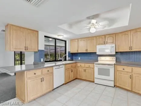 Kitchen featuring a tray ceiling, light brown cabinets, white appliances, and tasteful backsplash