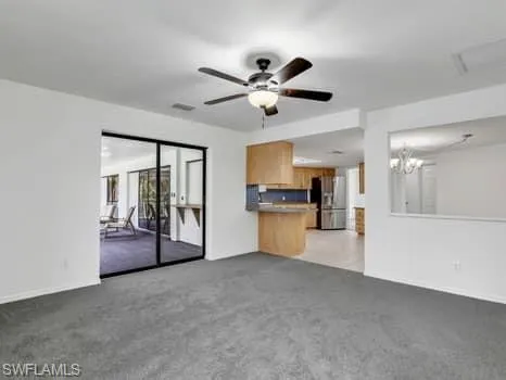 Unfurnished living room featuring light carpet, ceiling fan, and a chandelier