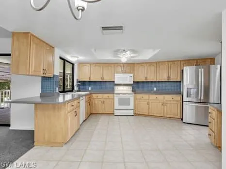 Kitchen featuring white appliances, tasteful backsplash, light brown cabinets, and a peninsula