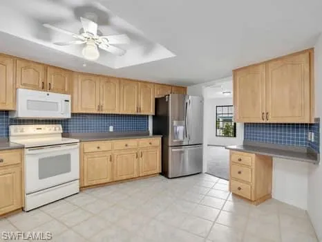 Kitchen featuring backsplash, white appliances, and light brown cabinetry