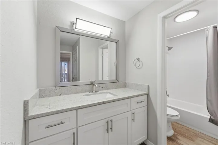 Bathroom featuring shower / bathtub combination with curtain, vanity, light wood-style floors, and a textured wall