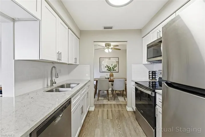 Kitchen featuring stainless steel appliances, backsplash, light stone countertops, and white cabinets