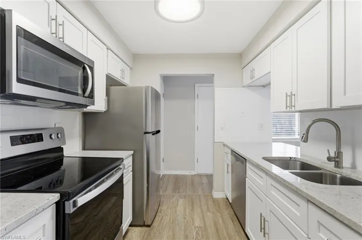 Kitchen featuring stainless steel appliances, tasteful backsplash, light stone countertops, white cabinets, and light wood-style flooring