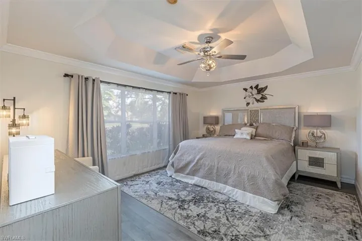 Bedroom featuring a tray ceiling, ornamental molding, wood finished floors, and a ceiling fan
