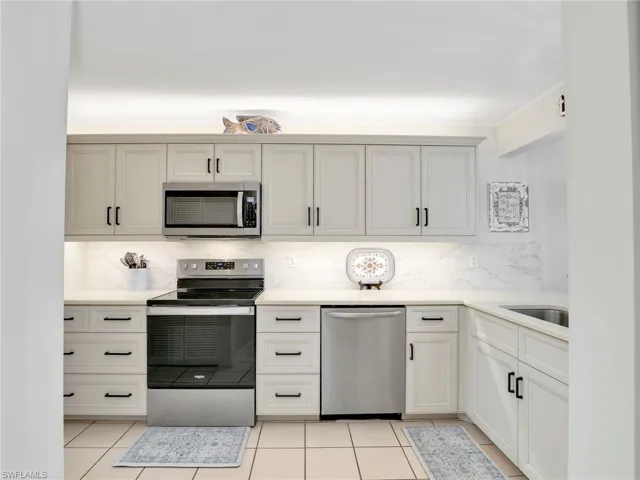 Kitchen with stainless steel appliances, backsplash, light countertops, and light tile patterned floors