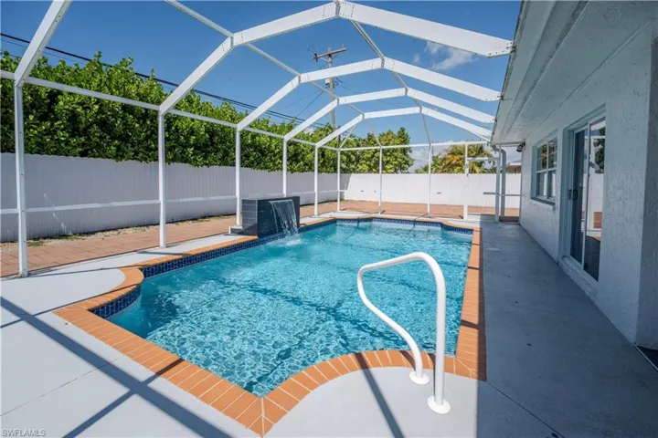 Screen-enclosed swimming pool featuring a waterfall accent and brick coping