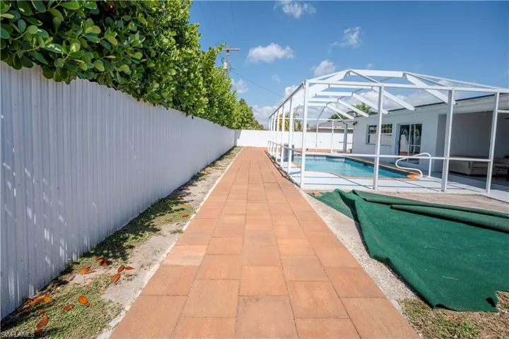 Expansive paver walkway alongside a tall white privacy fence with mature hedges