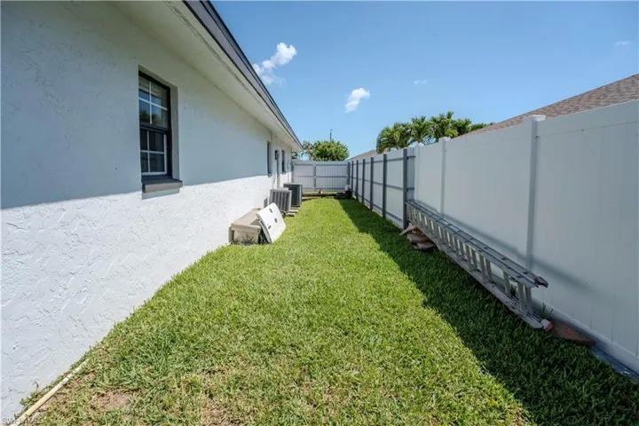 Side yard featuring a white stucco exterior, black-framed window, two exterior HVAC units, and a white privacy fence