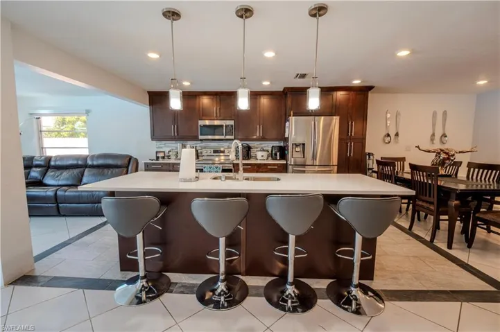 Open-concept kitchen featuring a spacious island with pendant lighting, dark wood cabinetry, a stainless steel refrigerator, and a tile backsplash