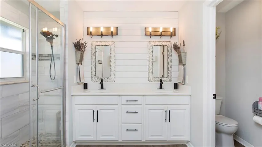 Bathroom with a shower with shower door, dual vanity, and toilet