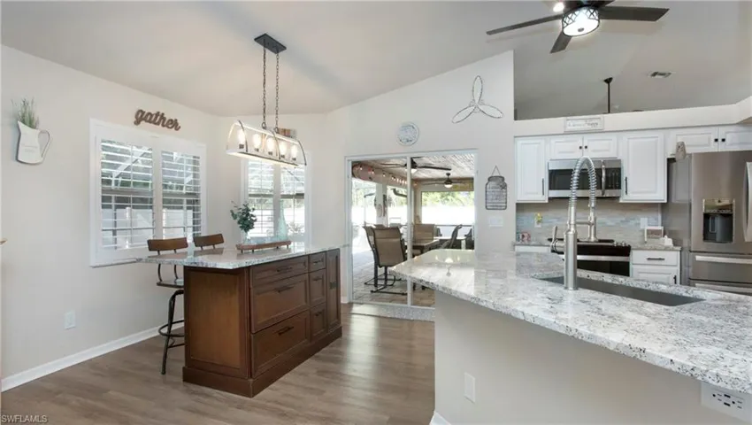 Kitchen featuring stainless steel appliances, light stone counters, white cabinetry, and hardwood / wood-style flooring