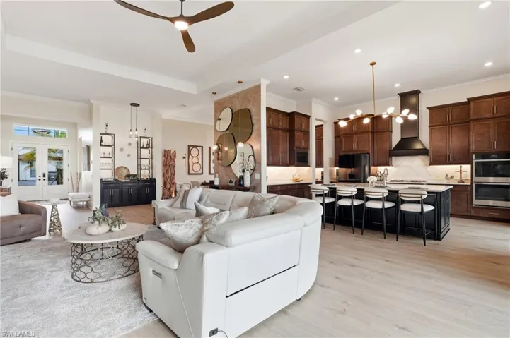 Living room featuring ornamental molding, light wood-style floors, a ceiling fan, a chandelier, and recessed lighting