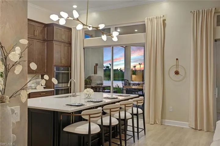 Kitchen with a breakfast bar area, light stone countertops, light wood-style floors, pendant lighting, and a kitchen island with sink