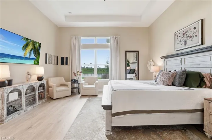 Bedroom with wood finished floors, a raised ceiling, and a water view
