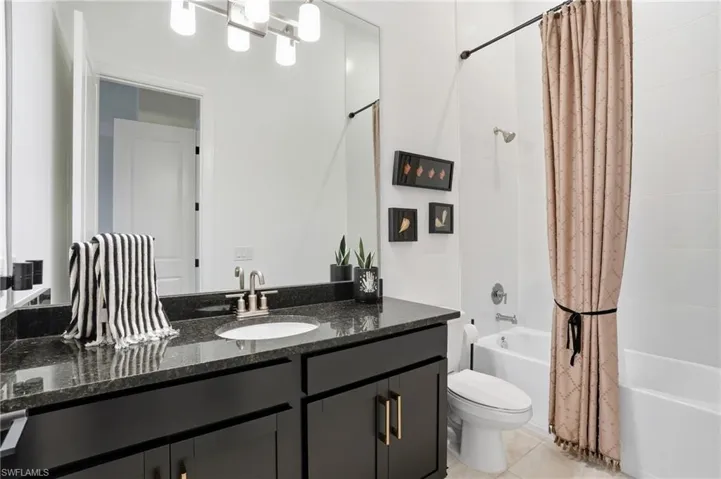 Bathroom featuring shower / tub combo with curtain, vanity, and light tile patterned flooring