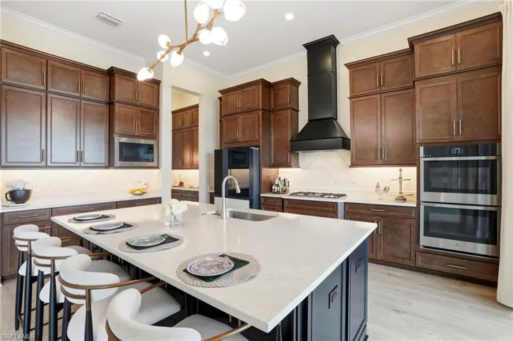 Kitchen featuring backsplash, ornamental molding, decorative light fixtures, light stone counters, and premium range hood
