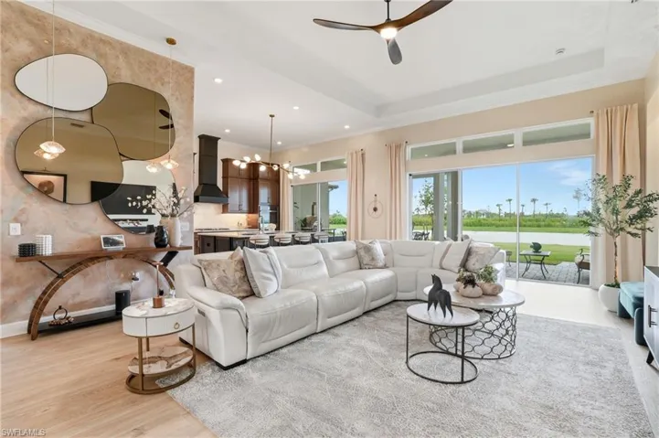 Living room featuring a tray ceiling, a chandelier, a ceiling fan, a water view, and recessed lighting