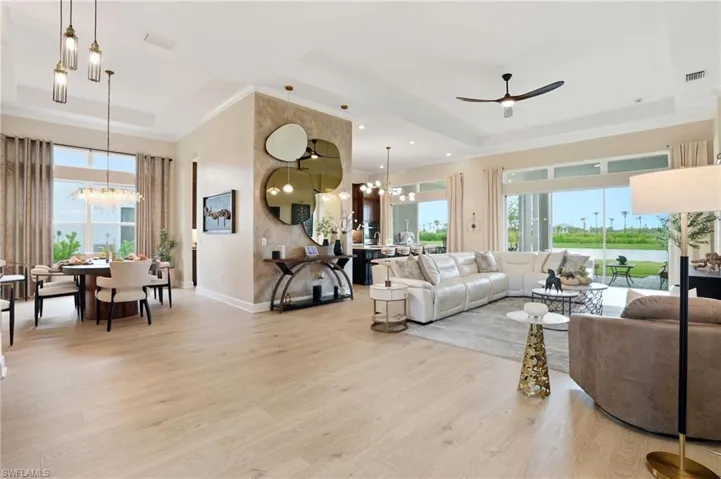 Living area featuring a tray ceiling, a chandelier, light wood-style flooring, ceiling fan, and ornamental molding