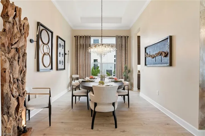 Dining room with light wood finished floors, ornamental molding, a chandelier, and a raised ceiling