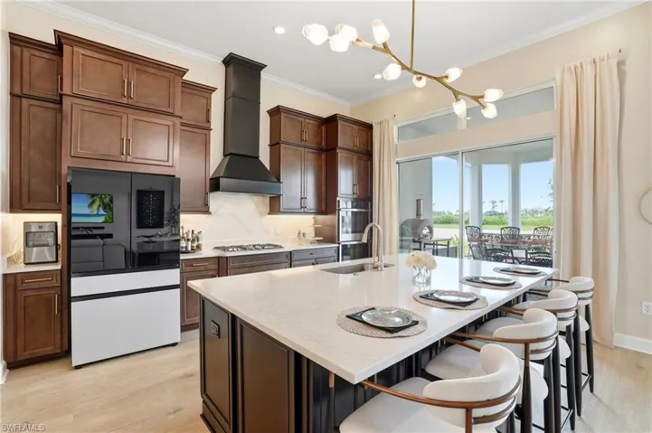 Kitchen featuring appliances with stainless steel finishes, crown molding, light wood-type flooring, light stone countertops, and decorative backsplash