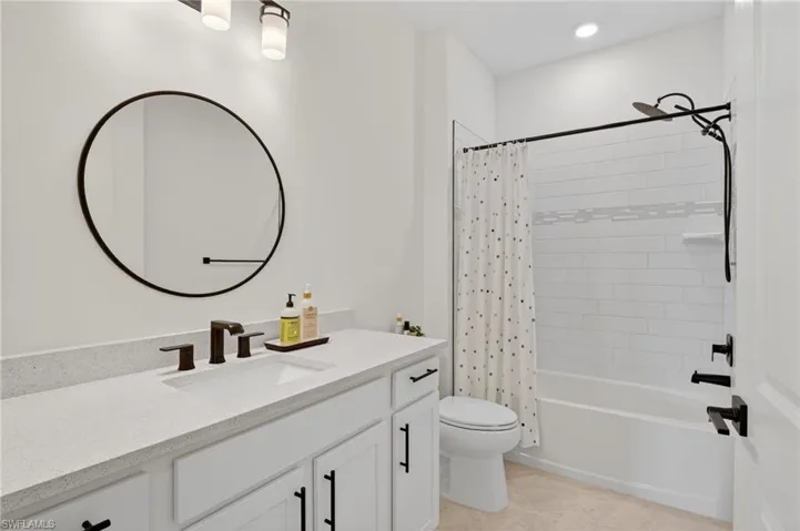 Bathroom featuring a white vanity with a light-toned countertop, a large circular mirror, and matte black fixtures