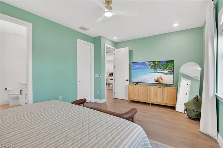 Spacious room with light wood-finish flooring, recessed lighting, a modern ceiling fan, and a white six-panel door leading to a half bath with a white vanity