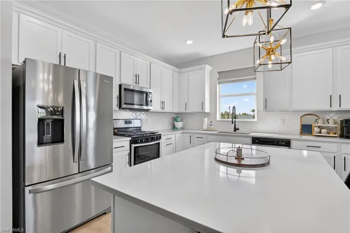 Contemporary kitchen featuring an expansive island with a light-colored countertop, white cabinetry with black hardware, stainless steel appliances, and a diagonal tile backsplash