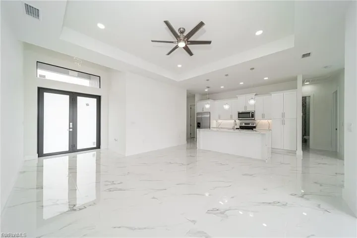 Unfurnished living room with a tray ceiling, french doors, recessed lighting, a ceiling fan, and light marble finish flooring