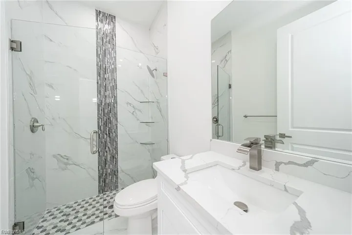Bathroom with a marble finish shower, vanity, and light marble finish flooring