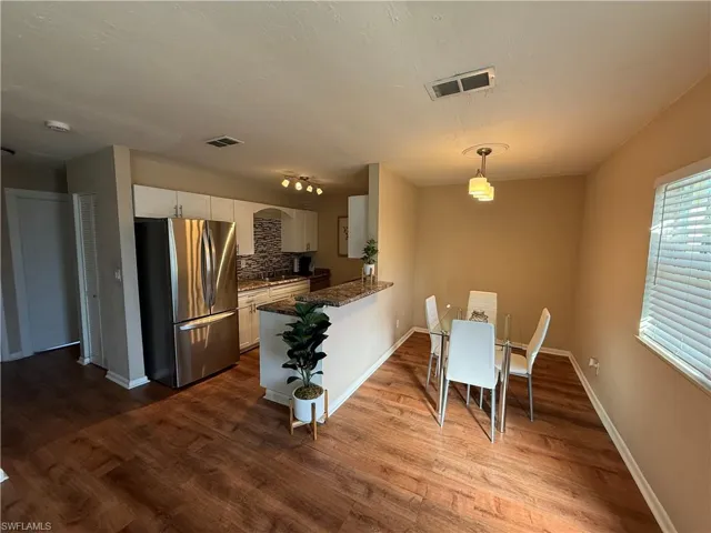 Kitchen featuring freestanding refrigerator, white cabinetry, pendant lighting, a peninsula, and dark stone countertops