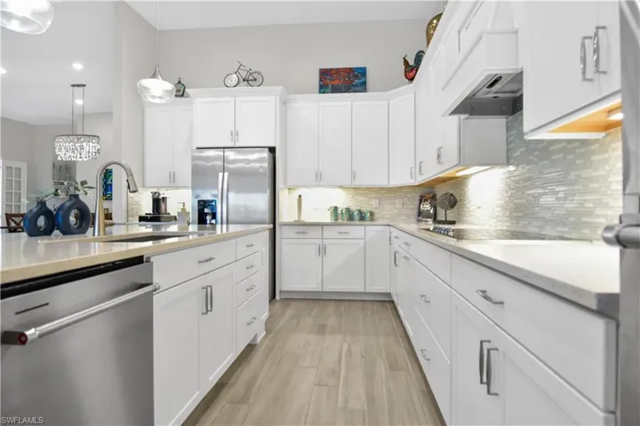 Kitchen with appliances with stainless steel finishes, decorative light fixtures, white cabinetry, and light hardwood / wood-style flooring
