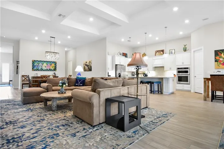 Living room with light hardwood / wood-style flooring, beamed ceiling, coffered ceiling, and an inviting chandelier