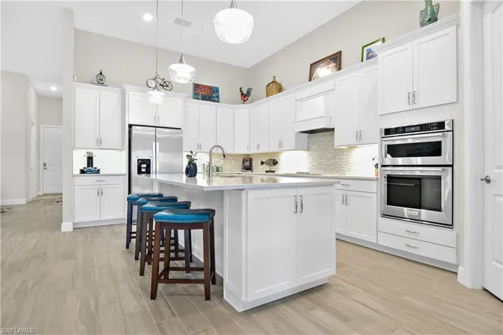 Kitchen with custom range hood, decorative light fixtures, white cabinetry, and stainless steel appliances