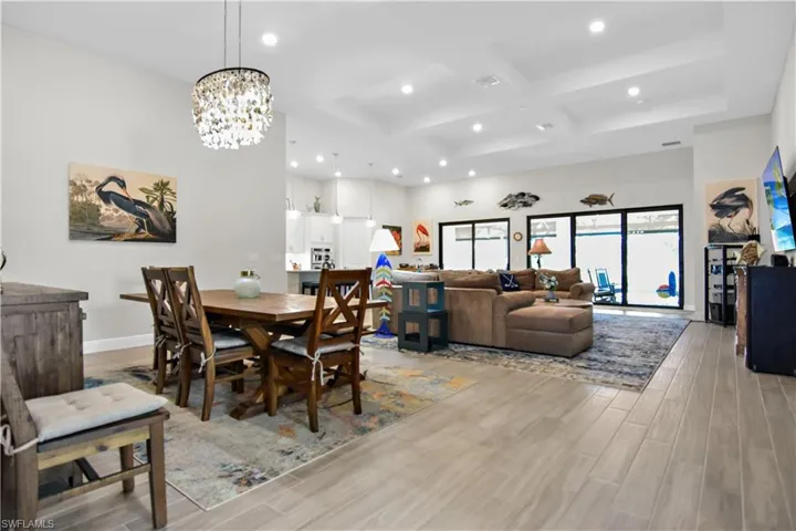 Dining room with beamed ceiling, light hardwood / wood-style floors, coffered ceiling, and an inviting chandelier