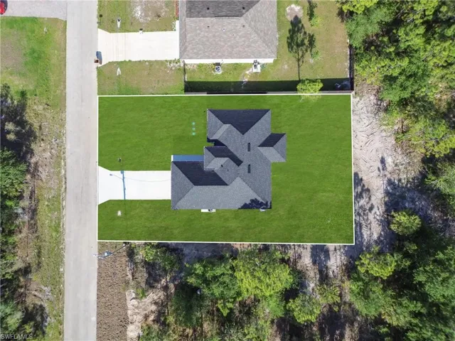 Aerial view showcasing a newly constructed property with a dark shingle roof and a verdant lawn