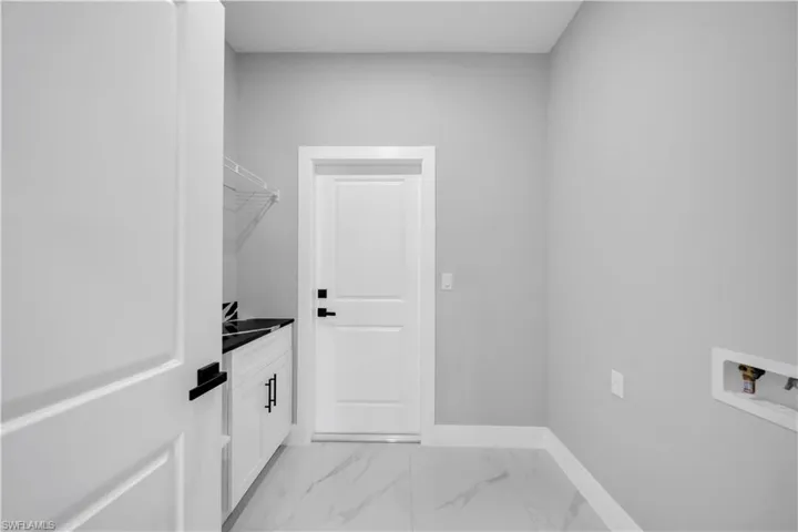 Utility room featuring white cabinetry with black hardware, a black countertop, and a utility sink