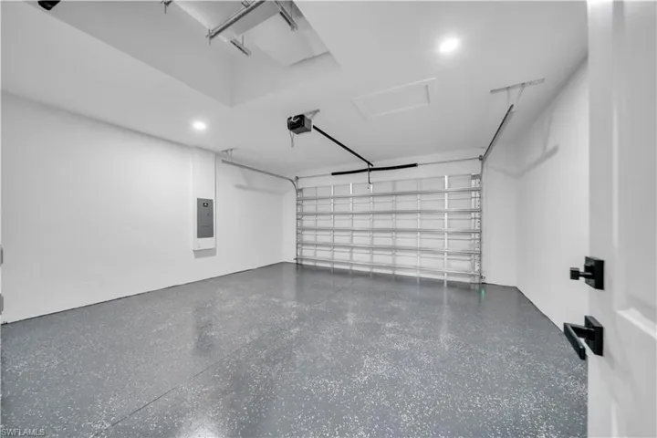 Spacious garage featuring a durable epoxy-coated floor, automatic garage door opener, recessed lighting, and a crisp white interior