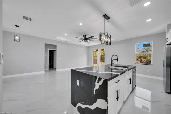 Open-concept living area featuring large format tile flooring, a kitchen island with a black and white patterned countertop, white cabinetry with matte black hardware, and a matte black gooseneck faucet