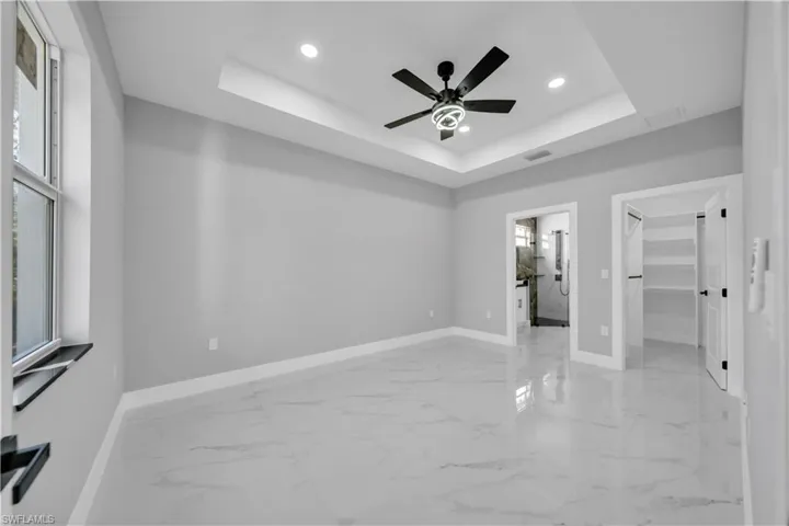 Spacious room featuring large format marble-look tile flooring, a tray ceiling with recessed lighting, and a modern black ceiling fan