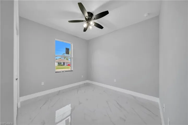 Spacious room featuring light gray walls, large format tile flooring, a window providing natural light, and a ceiling fan with integrated lighting