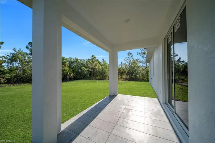 Covered patio with recessed lighting, large format tile flooring, and sliding glass doors opening to a spacious green lawn