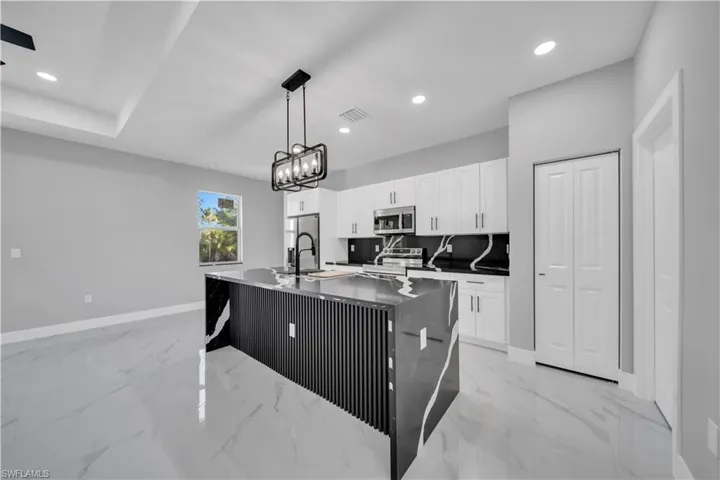 Kitchen featuring a large waterfall island with a black fluted panel base, white upper and lower cabinetry, and a black faucet