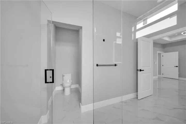 Bathroom featuring a glass-enclosed shower, marble-finish floor tiles, and a separate water closet