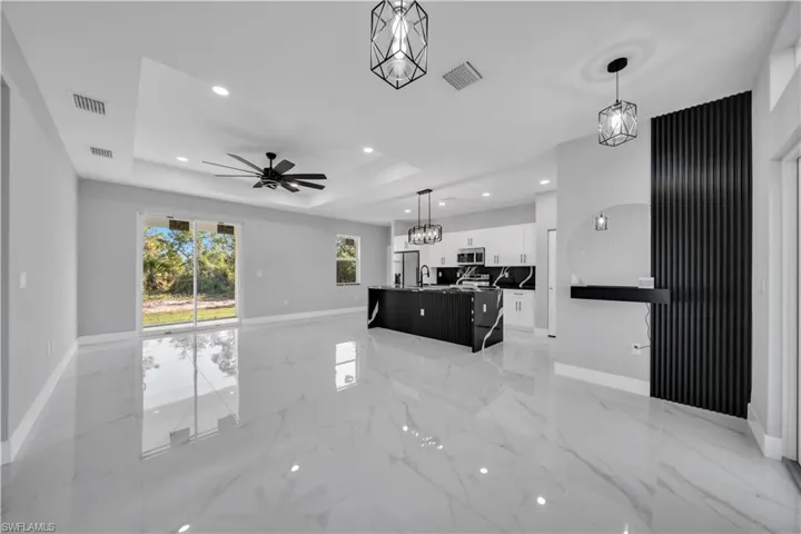 Spacious open-concept interior featuring light-toned large format tile flooring, a tray ceiling with recessed lighting and a ceiling fan, and sliding glass doors
