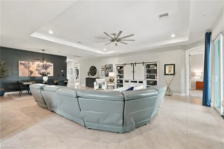 Open-concept living area featuring a tray ceiling, recessed lighting, tile flooring, built-in cabinetry with barn-style sliding doors, and a multi-blade ceiling fan