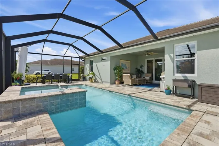 Screened-in pool area featuring a salt water pool with elevated spillover spa, stone-finish paver decking, and a spacious covered lanai