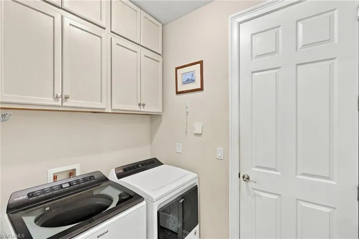 Laundry space featuring custom, white shaker-style wall-mounted cabinetry, a top-load washer, a front-load dryer, and a classic six-panel door to the garage