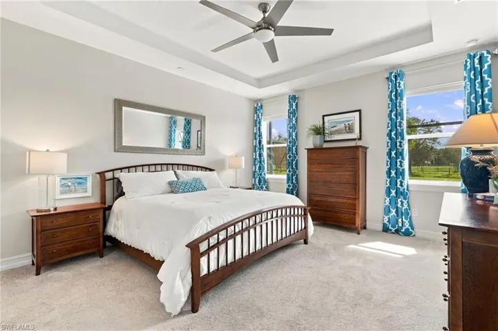Spacious primary bedroom featuring a recessed 10' tray ceiling, a central ceiling fan, and multiple windows providing natural lighting